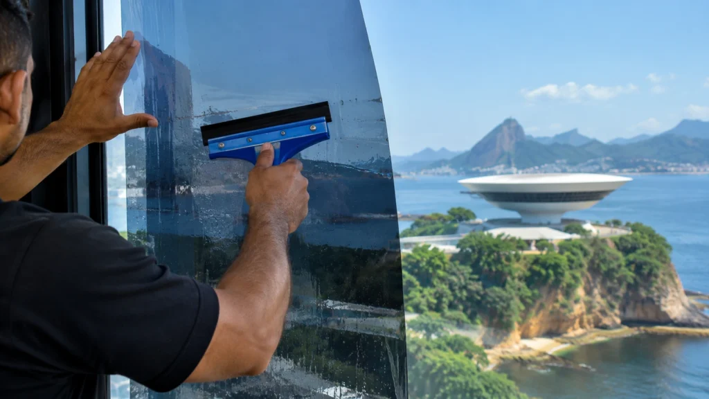 Profissional aplicando insulfilm residencial em janela com vista para o Museu de Arte Contemporânea de Niterói (MAC) ao fundo